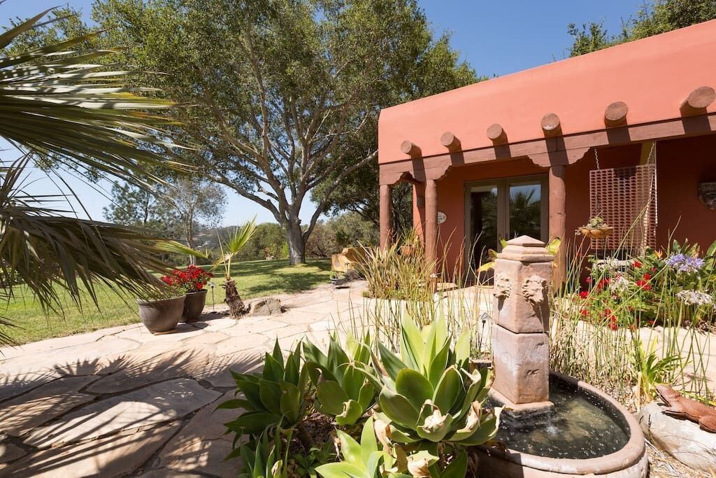 A garden with a water feature, potted plants, and a building with a distinctive red facade.