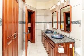 Un bagno moderno con mobili in legno, un doppio lavabo con lavelli in vetro blu, uno specchio grande e uno schienale rivestito di piastrelle.