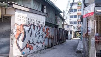 Ein schmaler Gang mit Graffiti an einer Wand, ein geschlossener Laden links und ein Gebäude mit einem Balkon rechts.