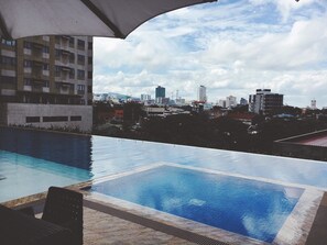 An infinity pool with a cityscape view, a covered seating area, and a modern building in the background. - The Persimmon Cebu by Sleepingpong (Cebu City)