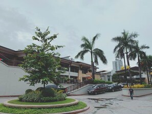 A building with a modern design, featuring a curved facade and a central staircase. There are palm trees and a well-maintained garden area. - The Persimmon Cebu by Sleepingpong (Cebu City)