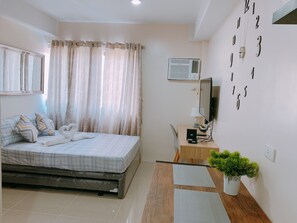 A bedroom with a bed, a desk, a TV, and a wall clock. - The Persimmon Cebu by Sleepingpong (Cebu City)