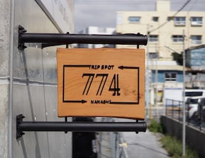 A wooden sign with the text "TRIP SPOT 7744" and "NANASHI" indicating a location. - Trip Spot 774 (Naha)