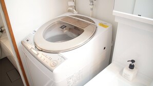 A front-loading washing machine in a bathroom with a white sink and a bottle of hand soap. - Trip Spot 774 (Naha)