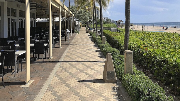 Een restaurant aan zee met terras, een verhard pad en uitzicht op het strand.