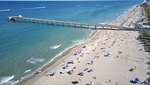 Een strand met een lange pier die in de oceaan uitloopt, veel parasols en een zandstrand.