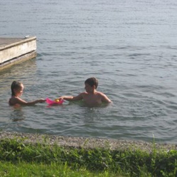 Two people in a body of water, possibly a lake or river, with a concrete dock in the background.