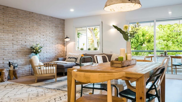 A modern living room with a brick wall, a wooden dining table, and a large window offering a view of greenery. - Sitges Colonial - Downtown near the Beach (Sitges)