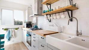 A modern kitchen with white cabinetry, a wooden countertop, a built-in stove, a sink, and a window providing natural light. - Sitges Colonial - Downtown near the Beach (Sitges)
