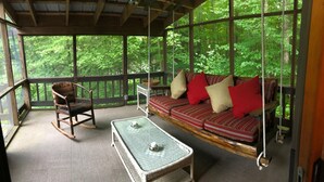 A covered porch with a swing seat, rocking chair, and wicker table.