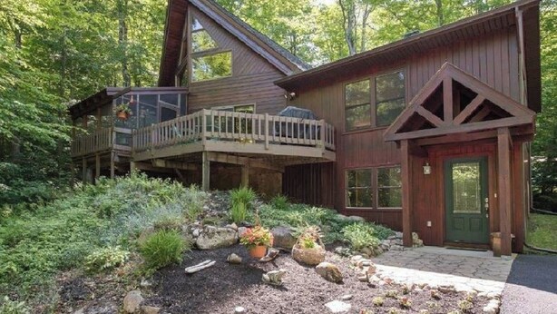 A wooden cabin with a balcony, surrounded by dense forest.