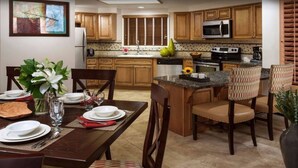 A modern kitchen with wooden cabinets, a central island, and a dining area set for a meal. - Welk Resort Villas - Winter Wonderland Weekend (Escondido)