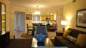A living room with a sofa, coffee table, and a blue vase. There is a dining area with chairs and a table in the background. - Welk Resort Villas - Winter Wonderland Weekend (Escondido)