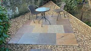 Un espace patio extérieur avec deux chaises en métal et une table en verre, entouré de carreaux de pierre et de galets.