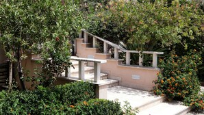 Una escalera con barandilla color beige, rodeada de abundante follaje y flores naranjas.