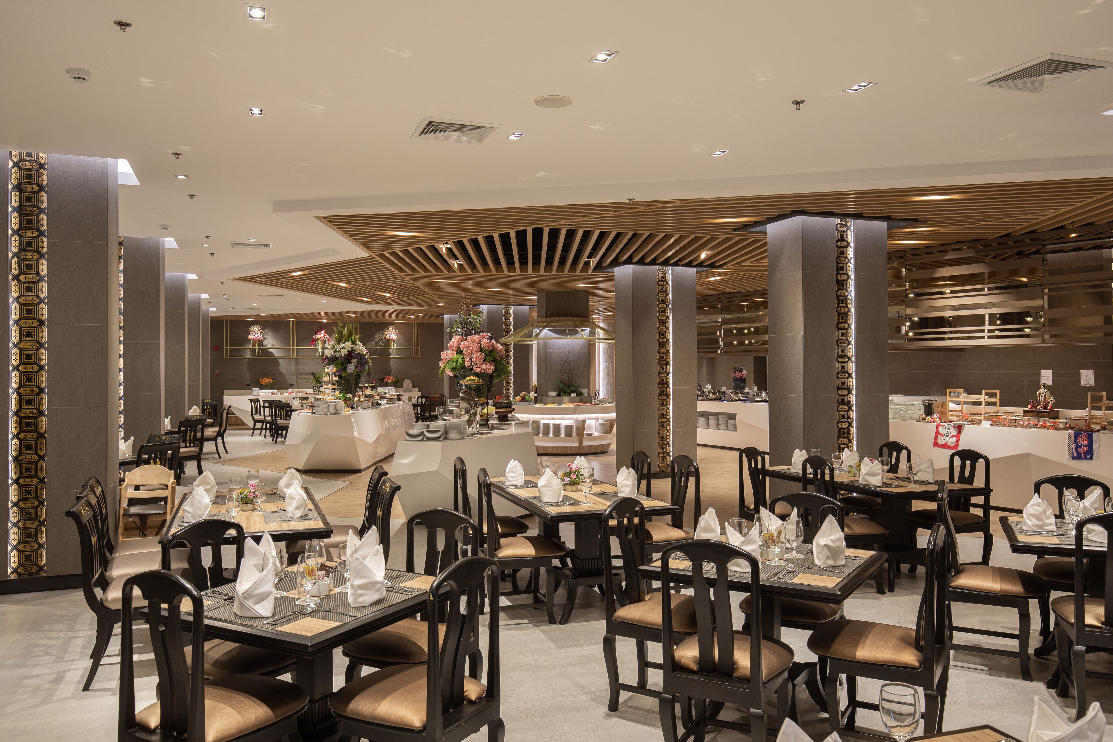 A modern dining area with tables set for service, a central counter, and decorative floral arrangements.