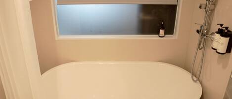 A modern bathroom with a freestanding bathtub, a window above the tub, and a showerhead.