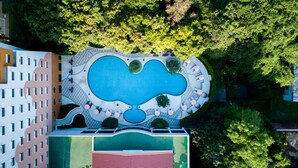 An aerial view of a hotel with a large central pool, surrounded by lounge areas and greenery.