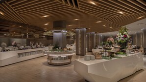 A modern hotel lobby with a central reception desk, a large decorative fountain, and a high ceiling with wooden paneling.