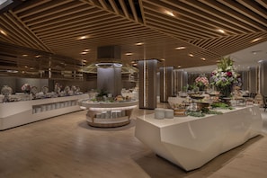 A modern hotel lobby with a central reception desk, a large decorative fountain, and a high ceiling with wooden paneling.