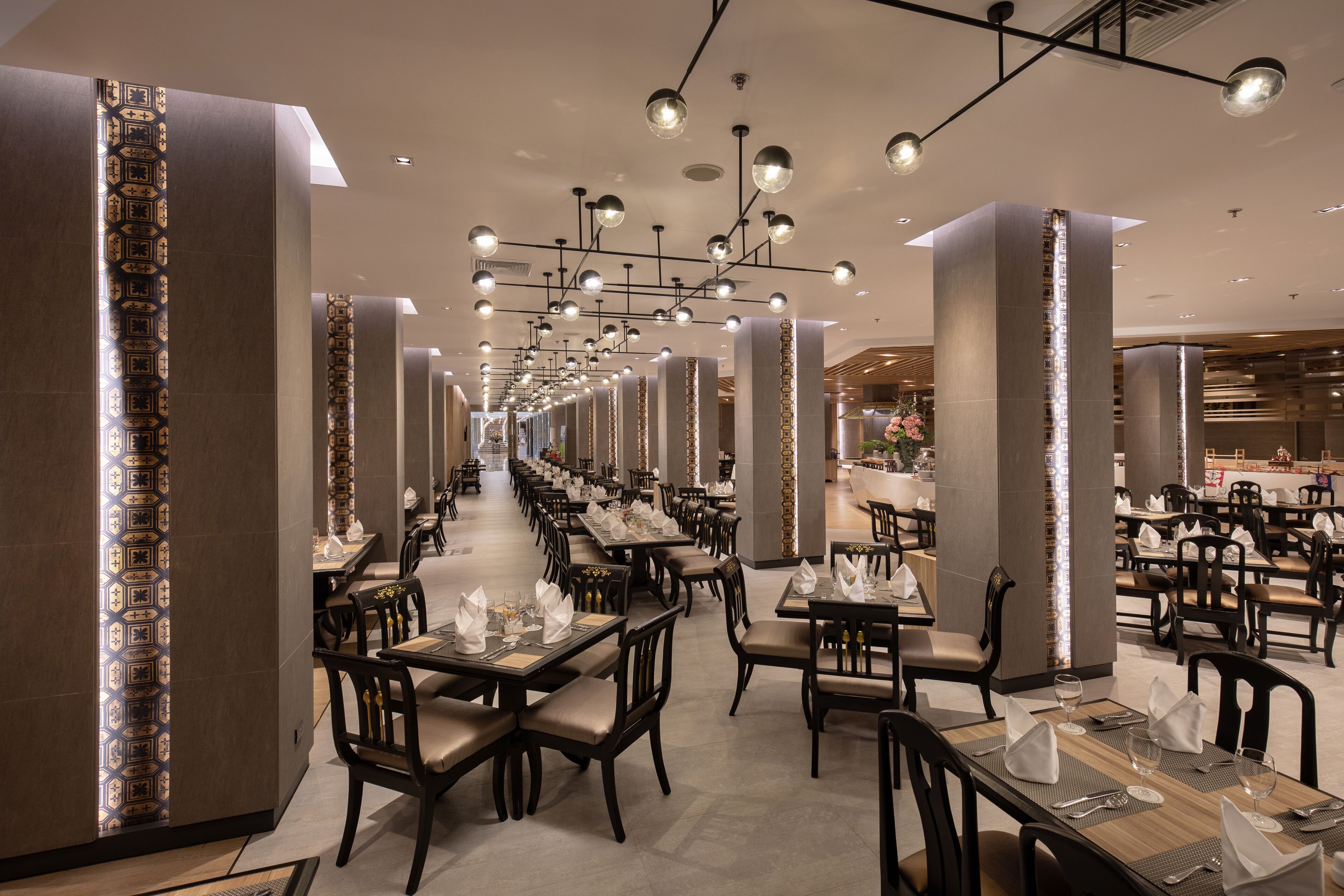 A spacious, modern restaurant with long tables and chairs, elegant lighting, and a clean, contemporary design.