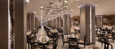 A spacious, modern restaurant with long tables and chairs, elegant lighting, and a clean, contemporary design.