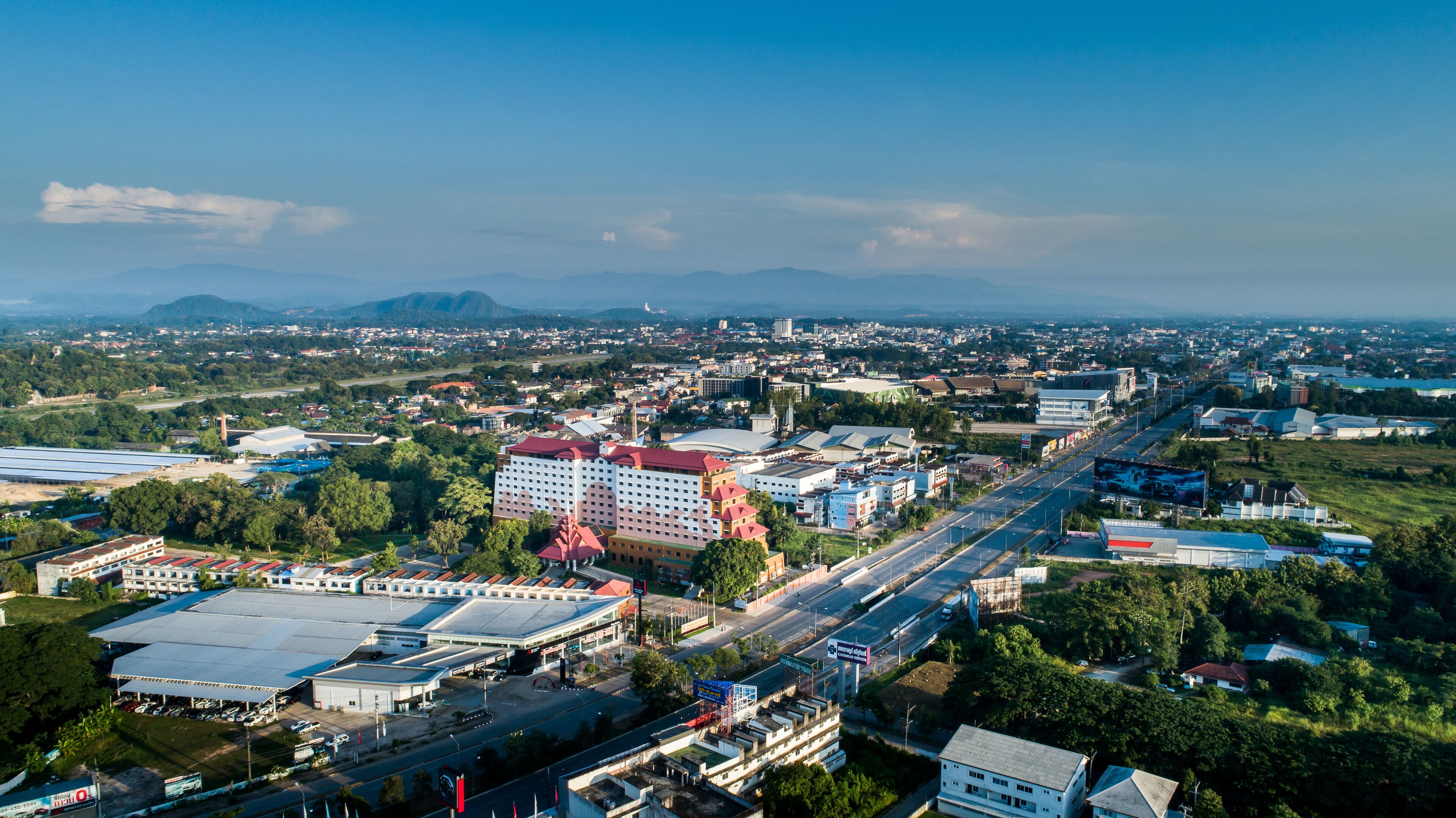Luftaufnahme einer Stadt mit einem markanten Hotel, das mehrere Stockwerke und ein rotes Dach aufweist, umgeben von Straßen und Grünflächen.