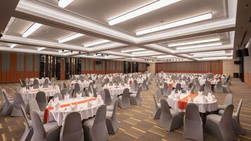 Une vaste salle de banquet, avec de longues rangées de tables rondes, chacune recouverte d’une nappe blanche et entourée de chaises grises.