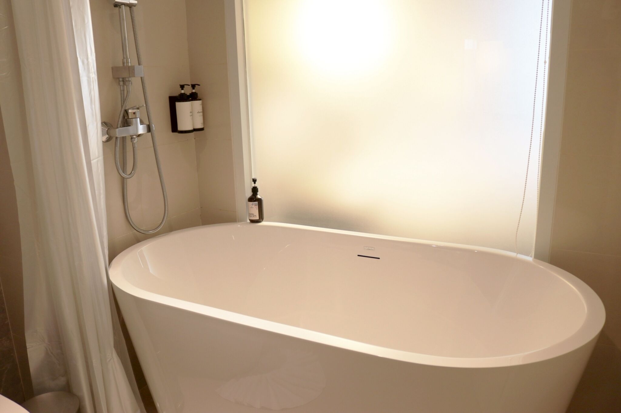 A modern bathroom with a freestanding bathtub, a showerhead, and a bottle of shampoo on the wall.