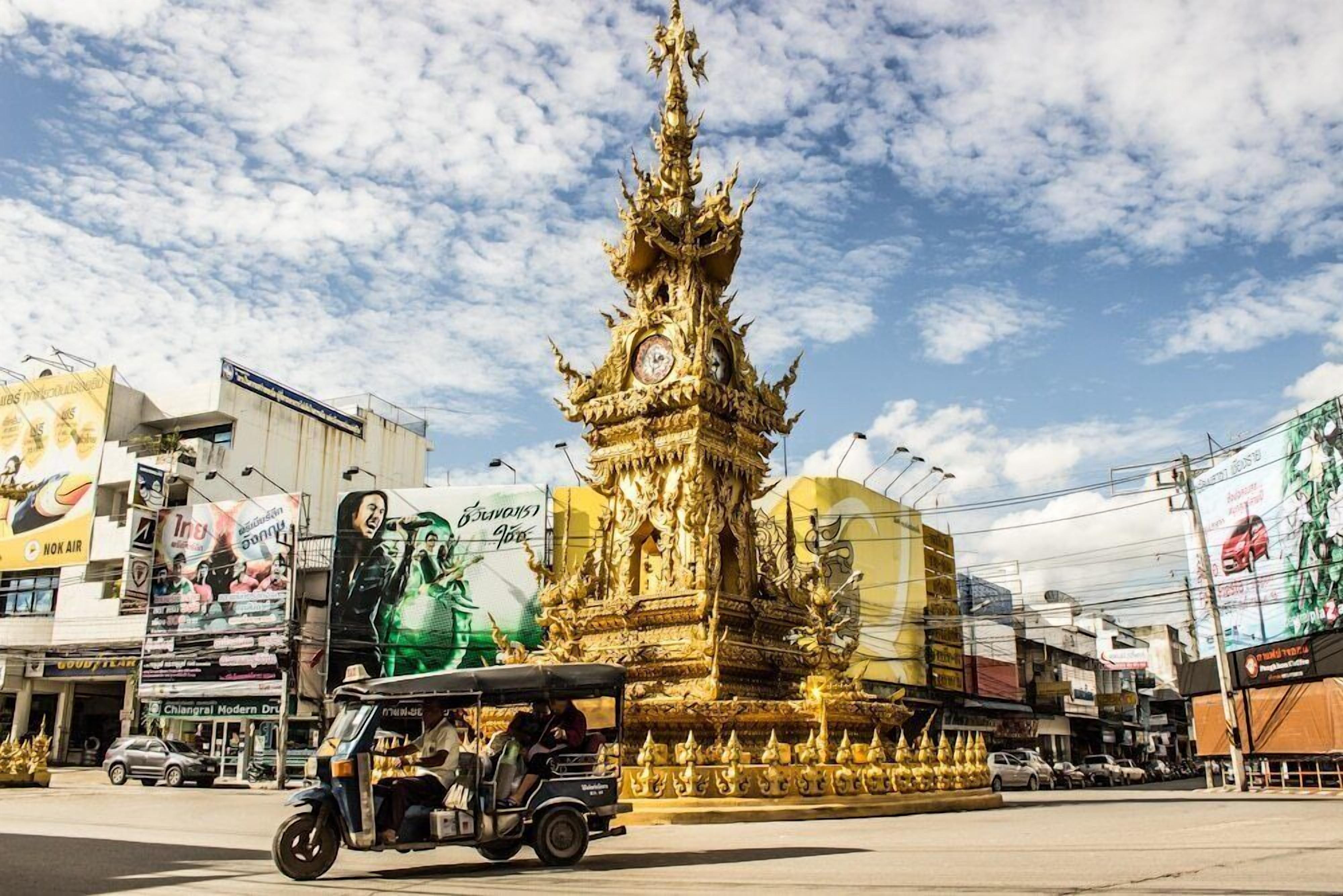 A golden stupa with a clock, surrounded by modern buildings and billboards.