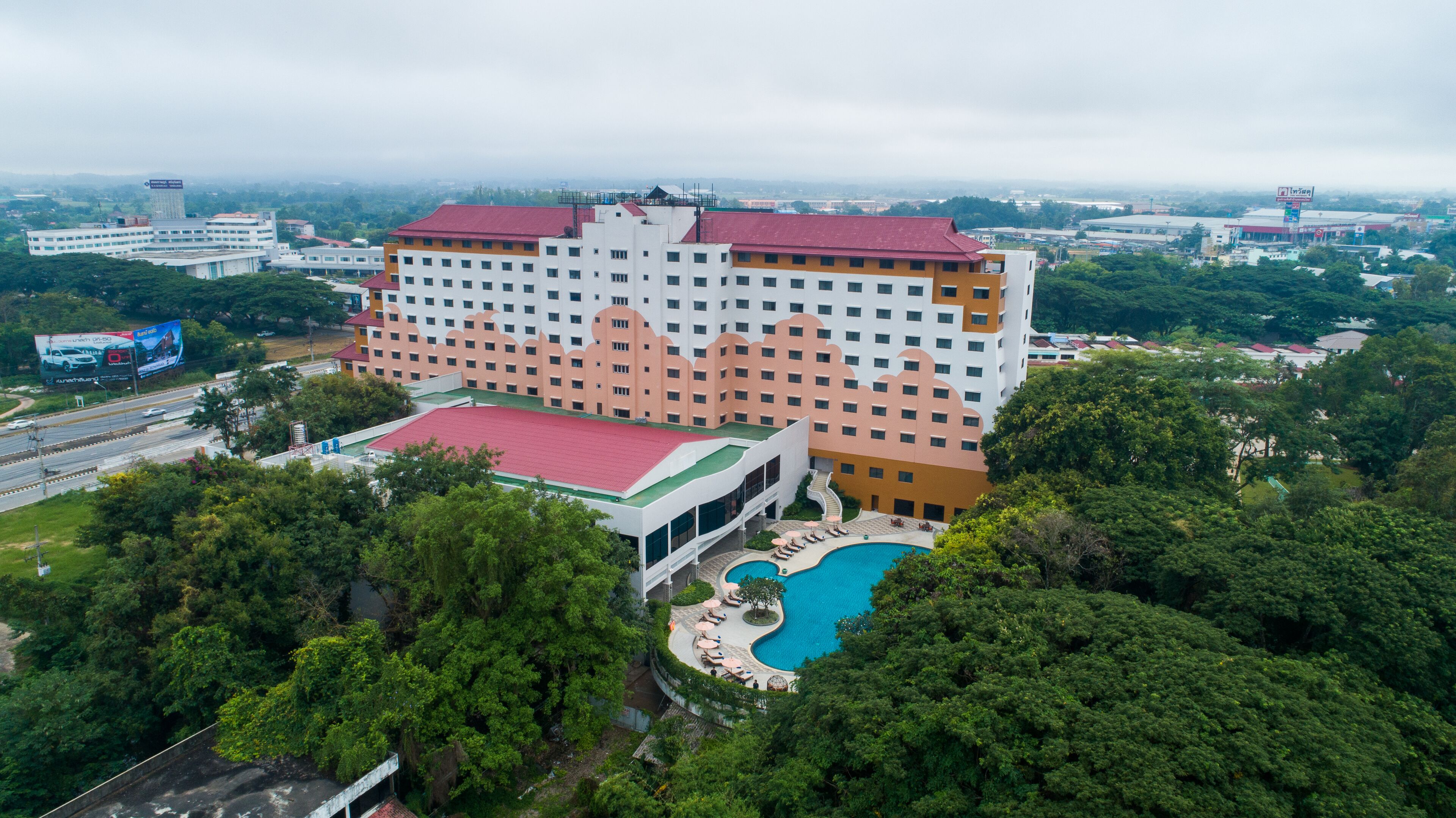 A large hotel with multiple floors, a swimming pool, and a parking area.