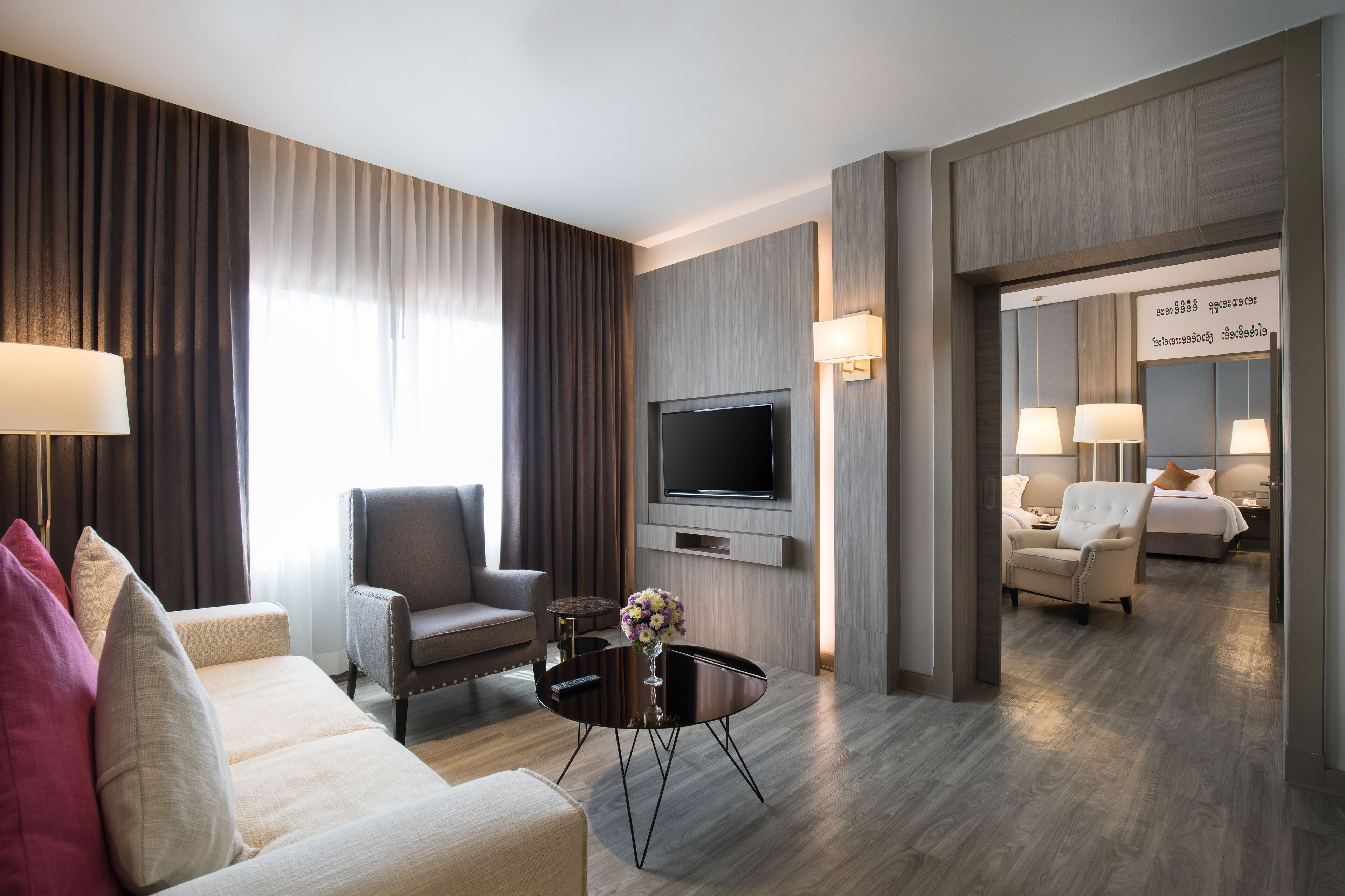 Habitación de hotel moderna con sofá, sillón, televisor y una mesita con un florero.