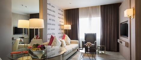 Una habitación de hotel moderna con una mesa de comedor de vidrio, un sofá, un televisor y un amplio ventanal con cortinas.