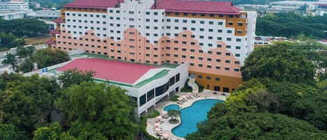 A hotel with multiple floors, a swimming pool, and lush greenery surrounding the property.