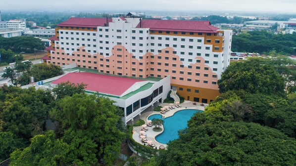 A hotel with multiple floors, a swimming pool, and lush greenery surrounding the property.