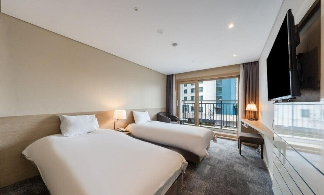 A hotel room with two beds, a TV, a balcony, and a city view.