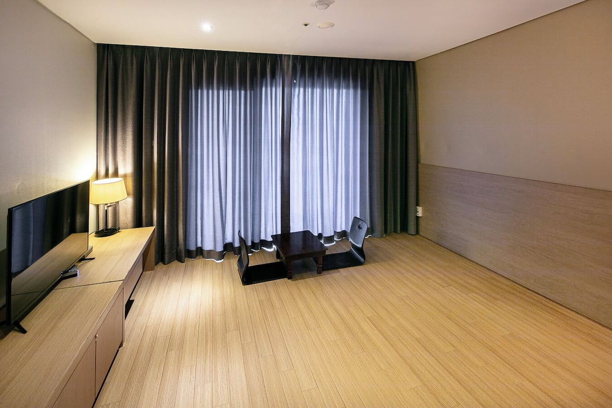 A hotel room with a bed, a desk with a lamp, a chair, and a large window with curtains.