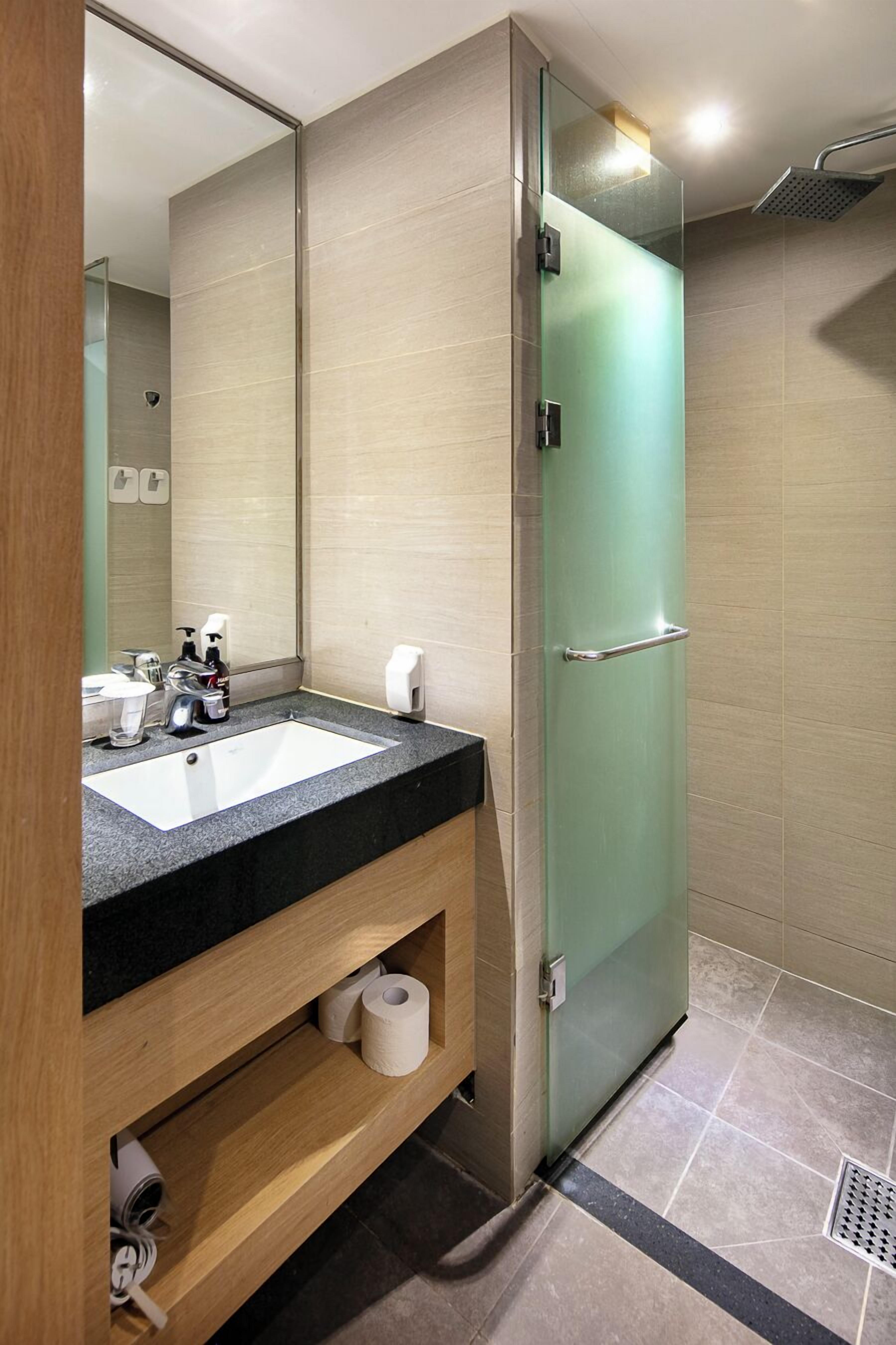A modern bathroom with a glass shower door, a sink with a black countertop, and a mirror.