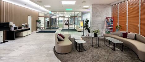 A modern lobby with a reception desk, seating area, and a large window with blinds.