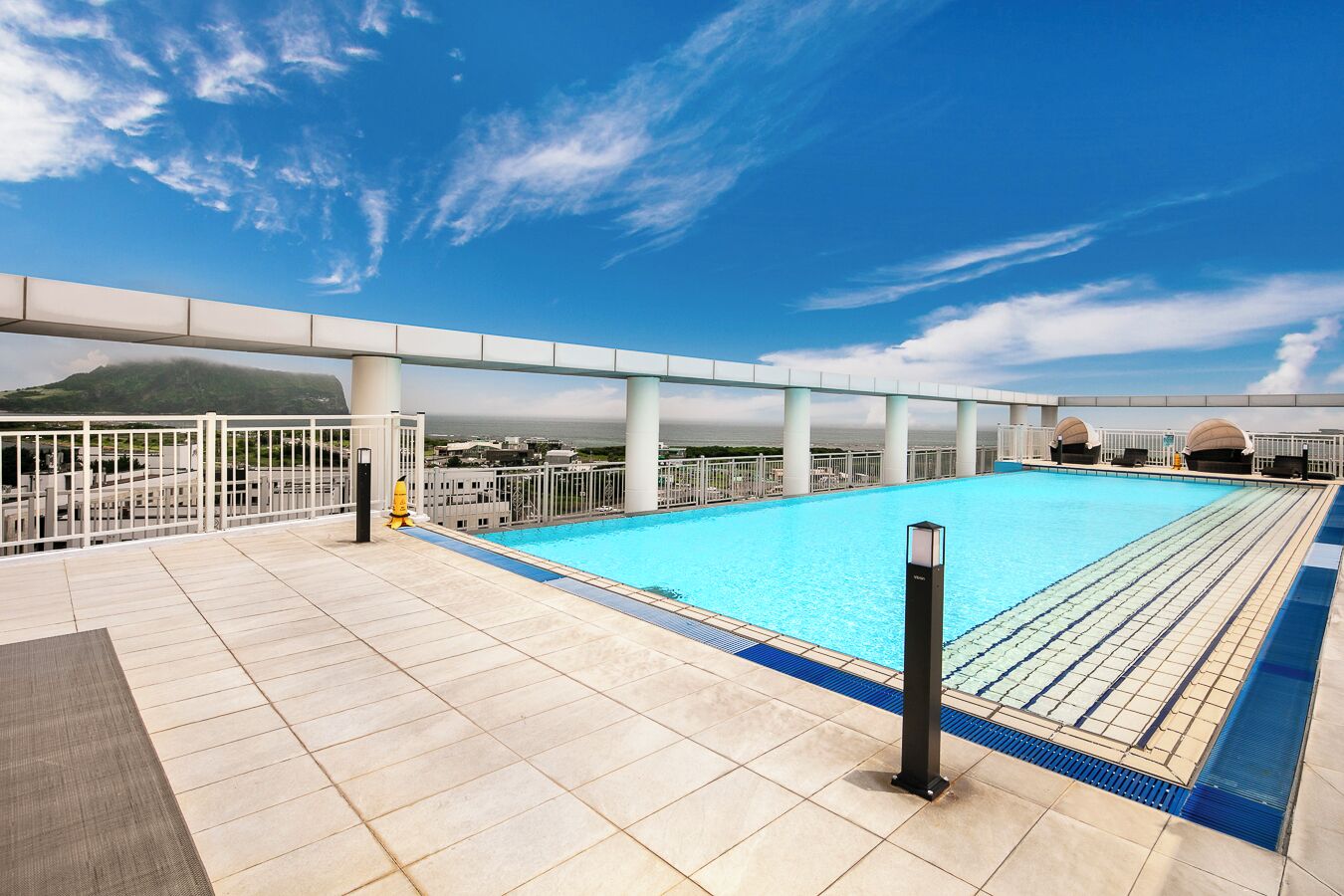 A rooftop swimming pool with a clear view of the ocean and a mountain in the background.