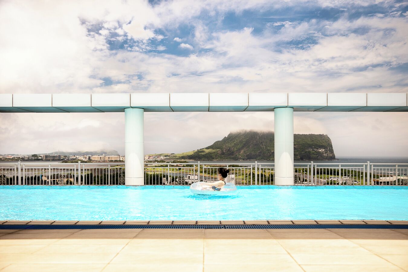 A pool with a view of a coastal landscape, including a hill and a body of water.