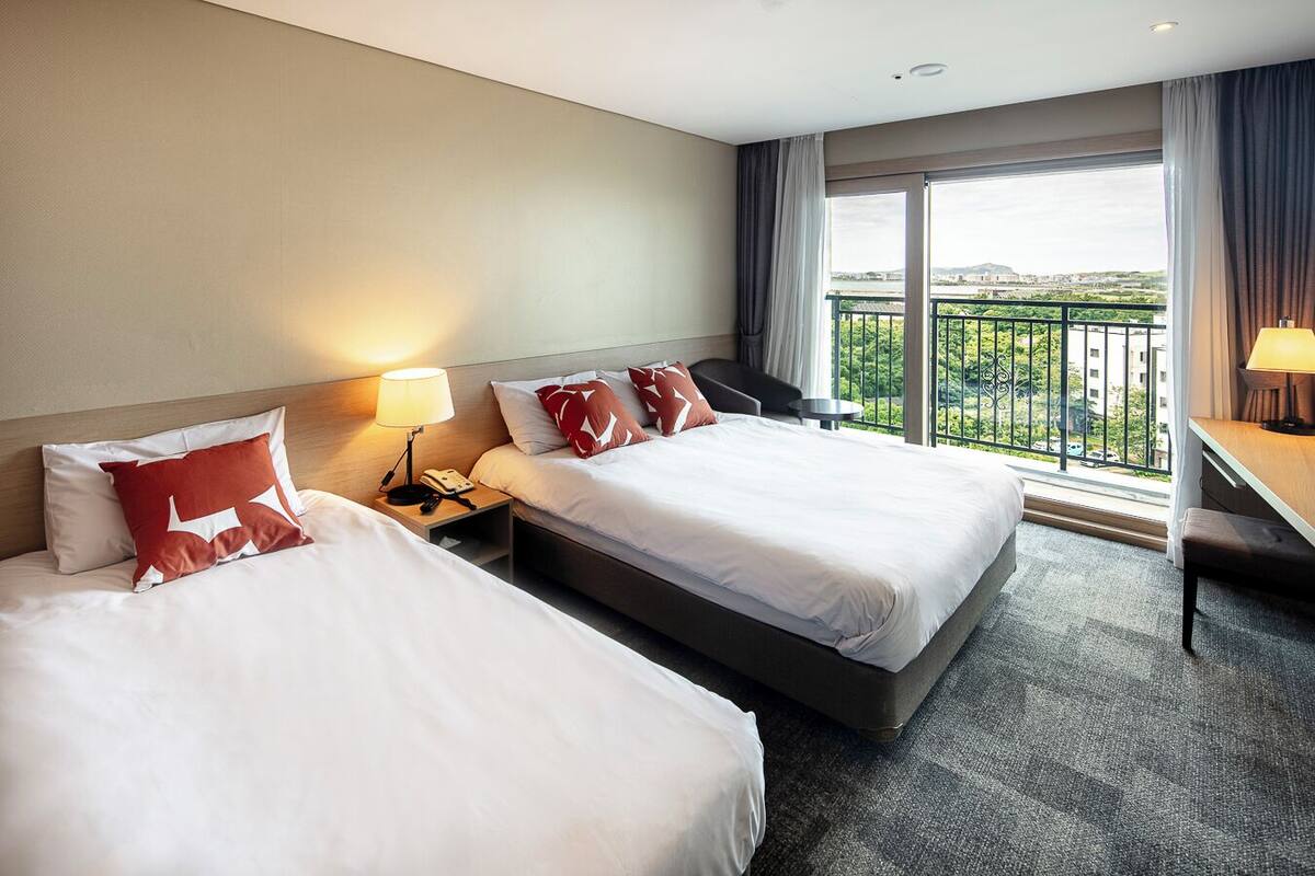 A hotel room with two beds, a desk, and a balcony with a view.