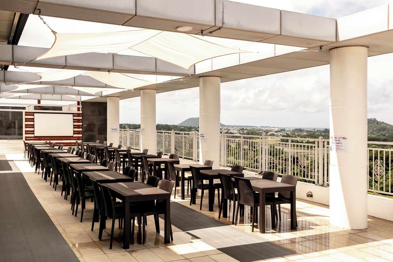 A covered outdoor seating area with tables and chairs, a whiteboard, and a view of the landscape.