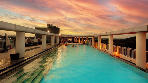 A swimming pool with a sunset view, supported by white pillars, and a railing on one side. - The Best Jeju Seongsan Hotel (Seogwipo)