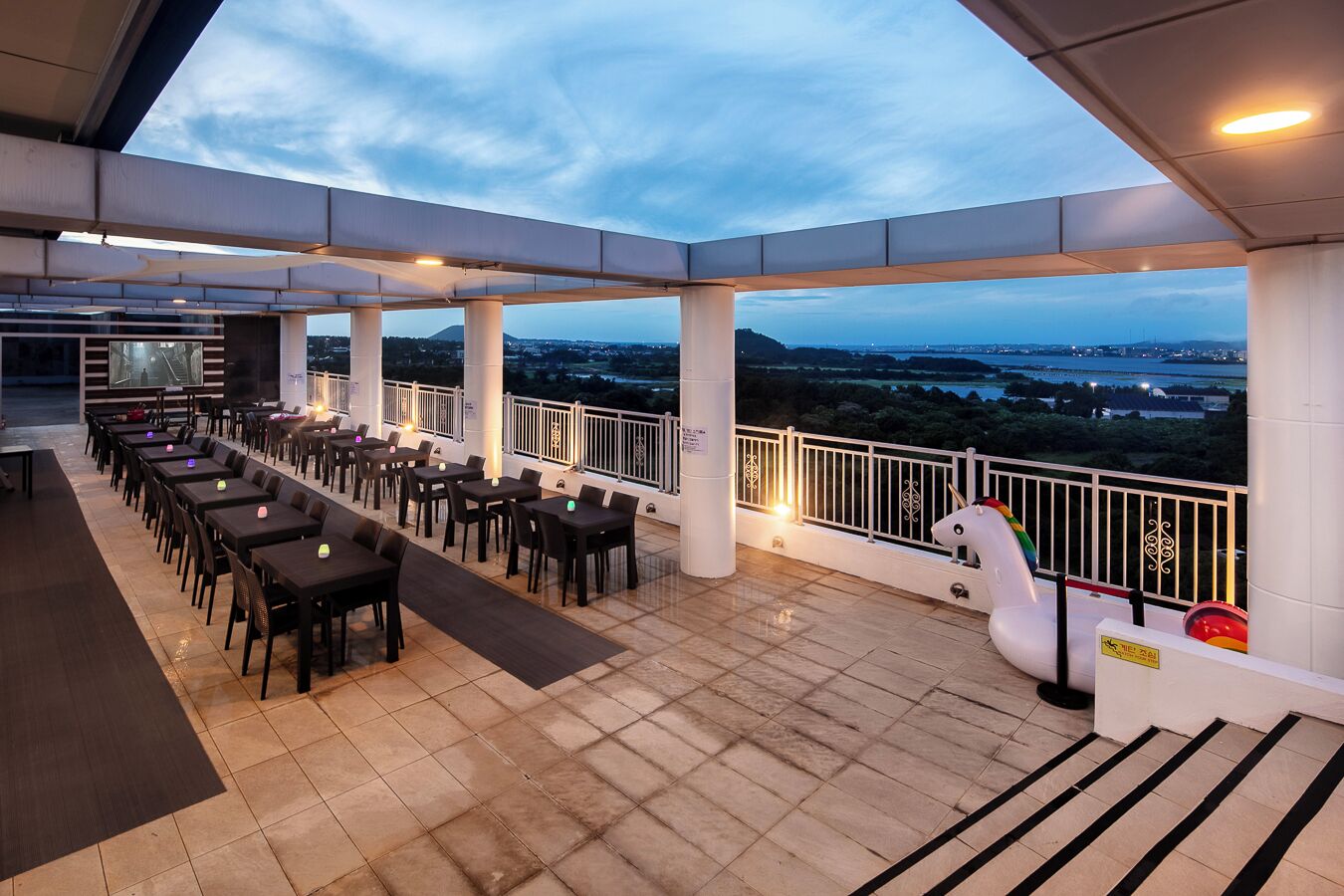 Un espace extérieur aménagé pour les repas, avec des tables et des chaises, une rambarde blanche et une vue sur le paysage.