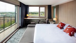 A hotel room with a large bed, a desk, a chair, a small table, and a view of the landscape through the window. - The Best Jeju Seongsan Hotel (Seogwipo)