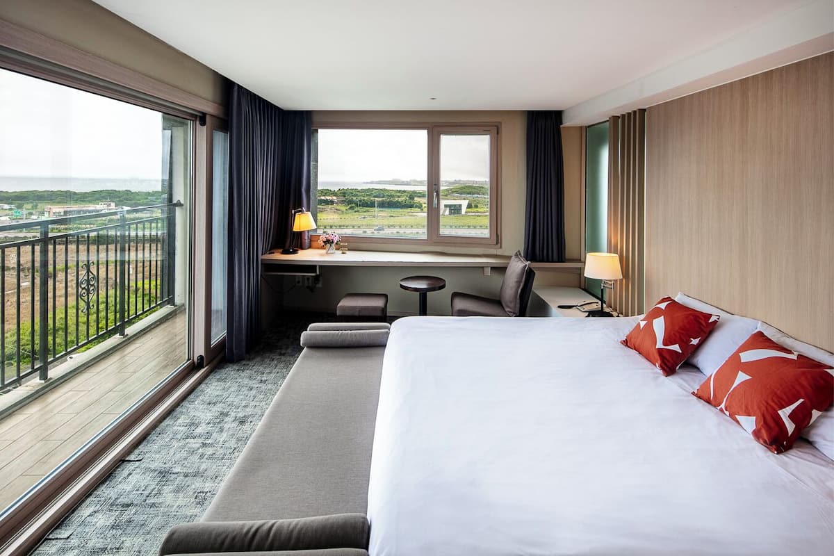 A hotel room with a large bed, a desk, a chair, a small table, and a view of the landscape through the window.