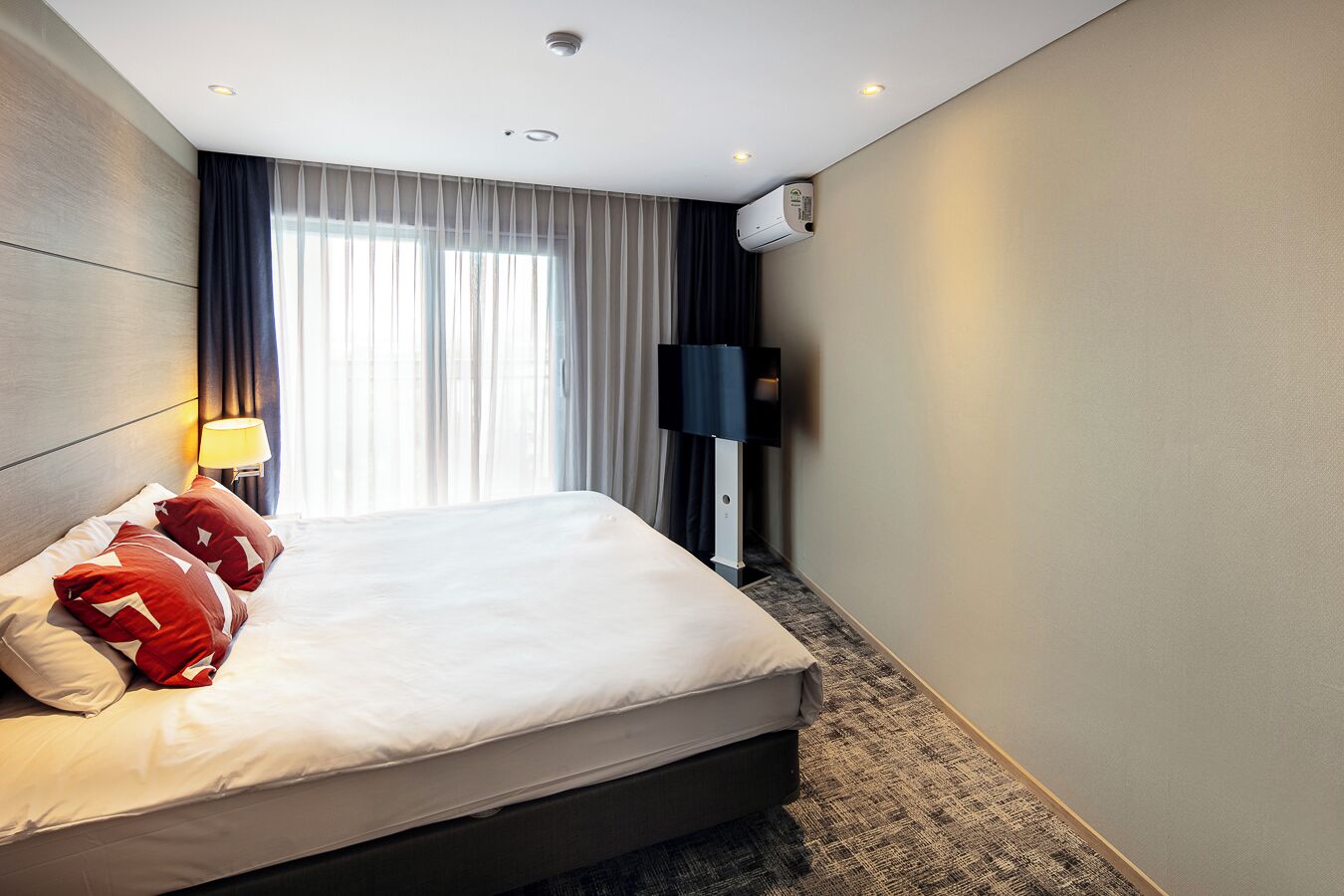 A hotel room with a bed, a TV mounted on the wall, and a window with curtains.