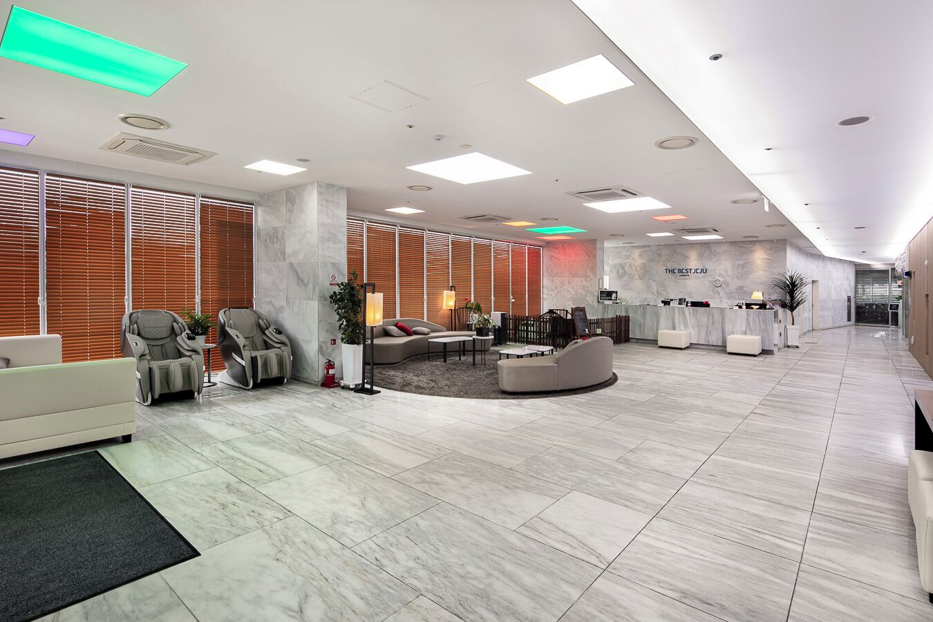 A spacious lobby with a reception desk, seating area, massage chairs, and a reception counter.