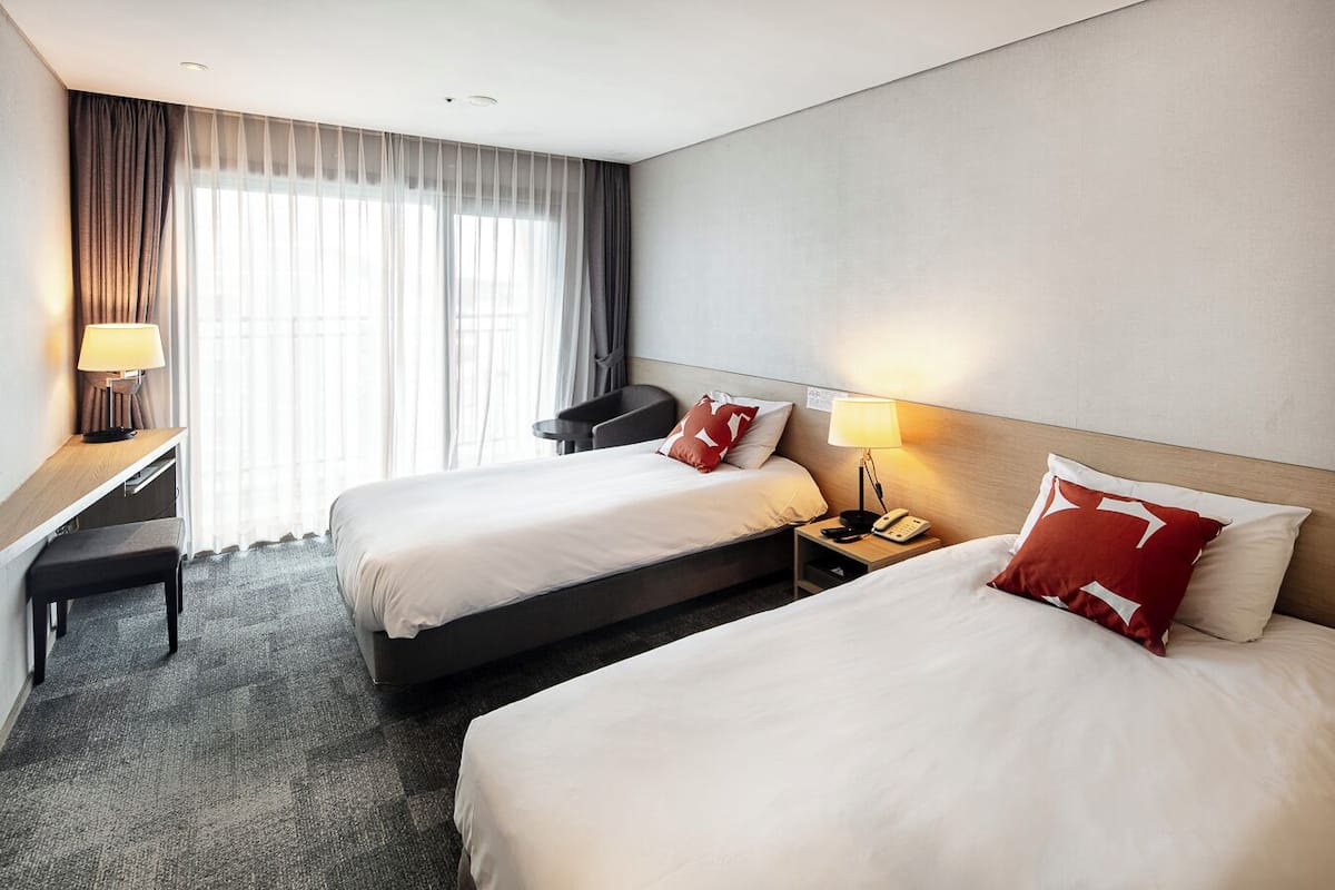 A hotel room with two beds, a desk, and a chair.